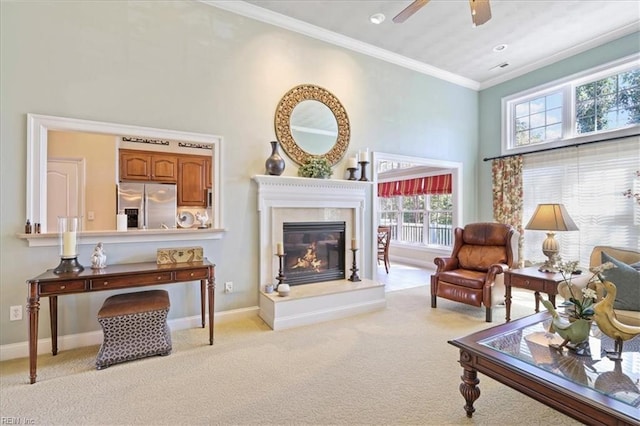 carpeted living area with ceiling fan, a high end fireplace, crown molding, baseboards, and a towering ceiling