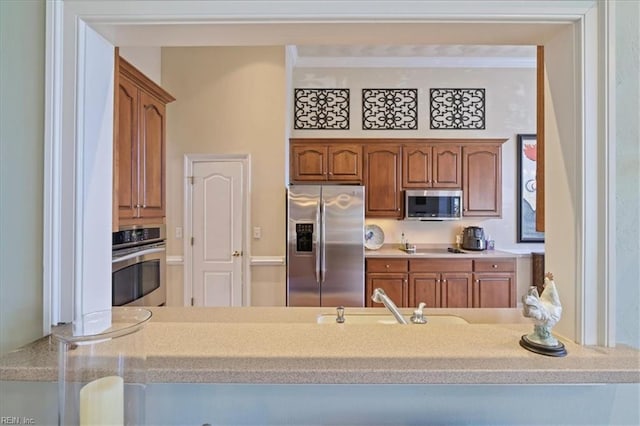 kitchen featuring light countertops, brown cabinets, appliances with stainless steel finishes, a peninsula, and a sink