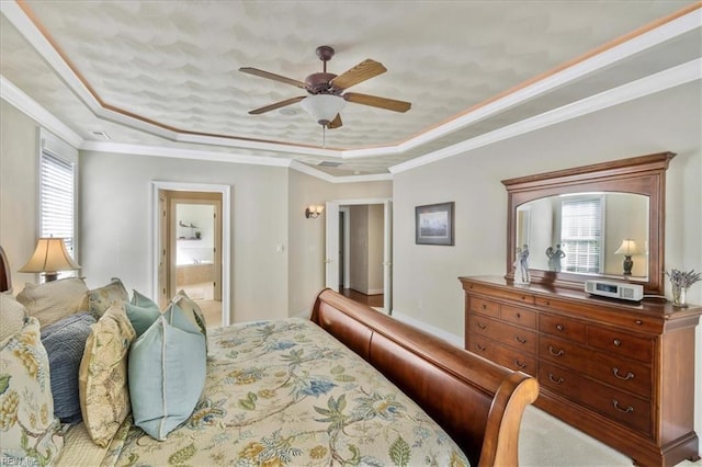 bedroom featuring ensuite bath, a ceiling fan, a tray ceiling, and ornamental molding