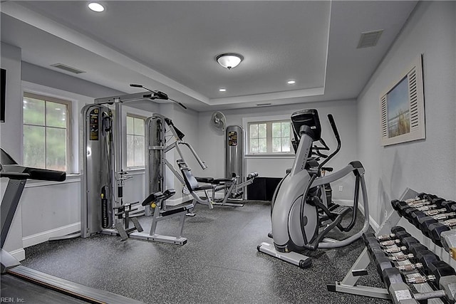 exercise room with a tray ceiling, visible vents, baseboards, and recessed lighting