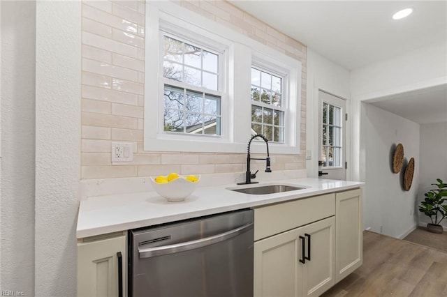 kitchen with decorative backsplash, wood finished floors, light countertops, stainless steel dishwasher, and a sink