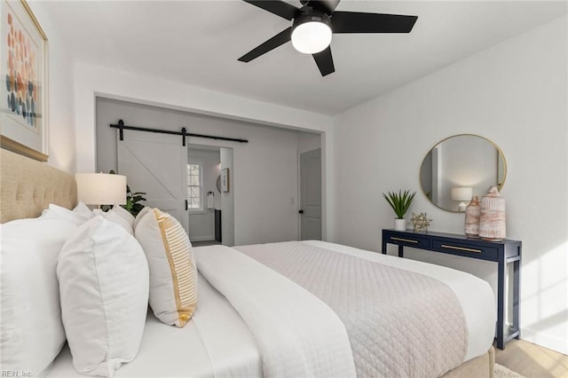 bedroom featuring a ceiling fan, wood finished floors, and a barn door