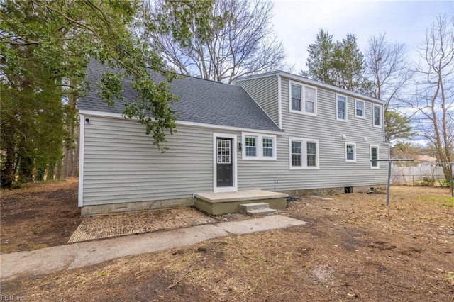 rear view of house featuring a shingled roof and fence