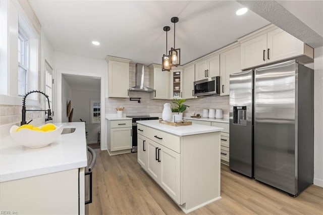 kitchen featuring light wood-style flooring, a sink, light countertops, appliances with stainless steel finishes, and wall chimney range hood