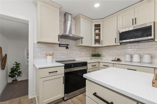 kitchen featuring decorative backsplash, electric stove, wall chimney exhaust hood, stainless steel microwave, and light countertops