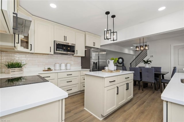 kitchen featuring tasteful backsplash, appliances with stainless steel finishes, wood finished floors, decorative light fixtures, and light countertops