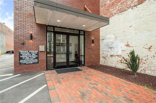 view of exterior entry featuring uncovered parking, french doors, and brick siding