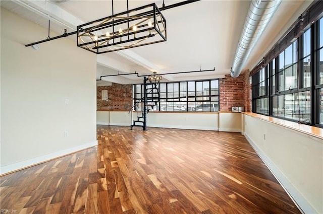 interior space with an inviting chandelier, baseboards, brick wall, and wood finished floors