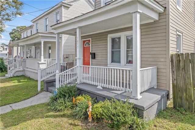 entrance to property with a porch, a yard, and fence