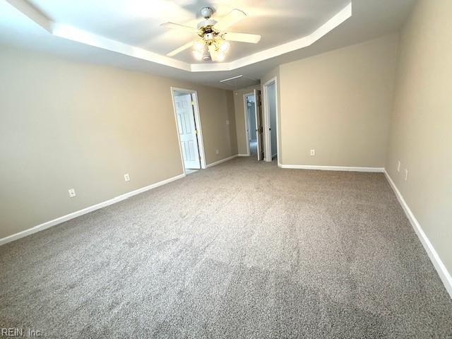 carpeted spare room with a tray ceiling, a ceiling fan, and baseboards