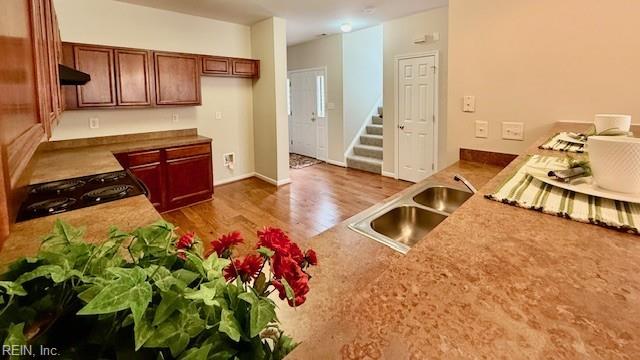 kitchen featuring under cabinet range hood, stove, wood finished floors, and a sink