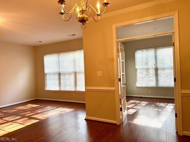 unfurnished room with a chandelier, ornamental molding, baseboards, and wood finished floors