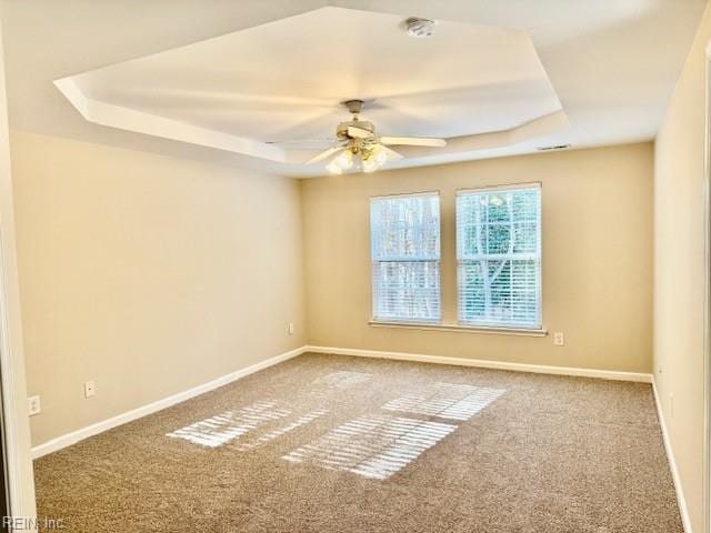 carpeted empty room with baseboards, a raised ceiling, and ceiling fan