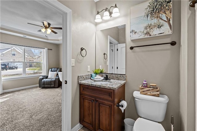 bathroom featuring baseboards, ceiling fan, toilet, a tray ceiling, and vanity