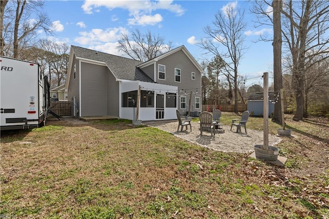 rear view of property featuring a fire pit, fence, a lawn, a sunroom, and a patio area