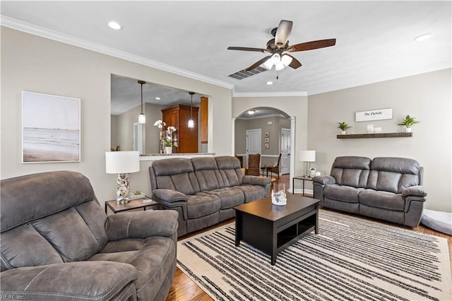 living area featuring wood finished floors, recessed lighting, arched walkways, crown molding, and ceiling fan