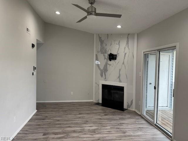 unfurnished living room featuring recessed lighting, a premium fireplace, wood finished floors, and a ceiling fan