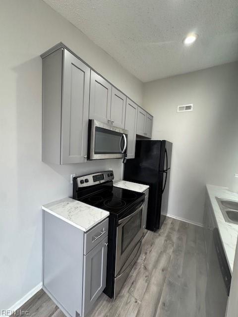 kitchen featuring visible vents, gray cabinets, a textured ceiling, light wood-style floors, and appliances with stainless steel finishes