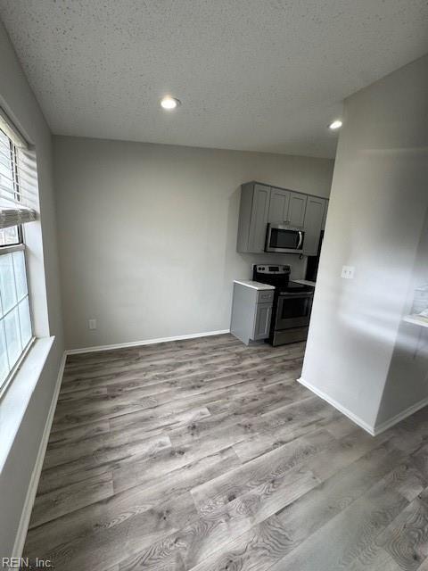 kitchen featuring wood finished floors, baseboards, gray cabinets, stainless steel appliances, and a textured ceiling