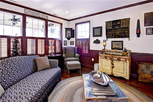 living area with ceiling fan, a wainscoted wall, wood finished floors, visible vents, and crown molding