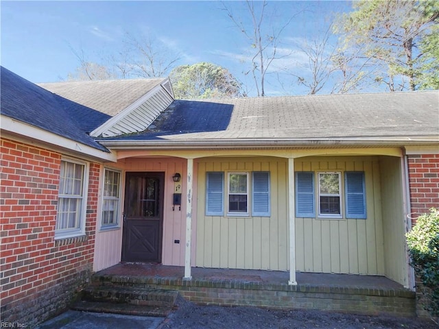 property entrance with roof with shingles, a porch, and brick siding