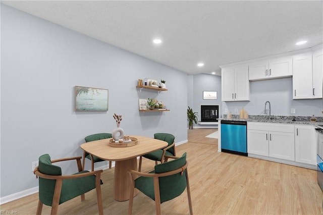 kitchen featuring dishwashing machine, a sink, white cabinets, light wood-type flooring, and a glass covered fireplace