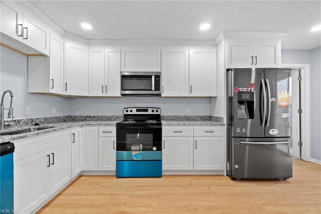 kitchen featuring appliances with stainless steel finishes, a sink, white cabinets, and light wood-style floors