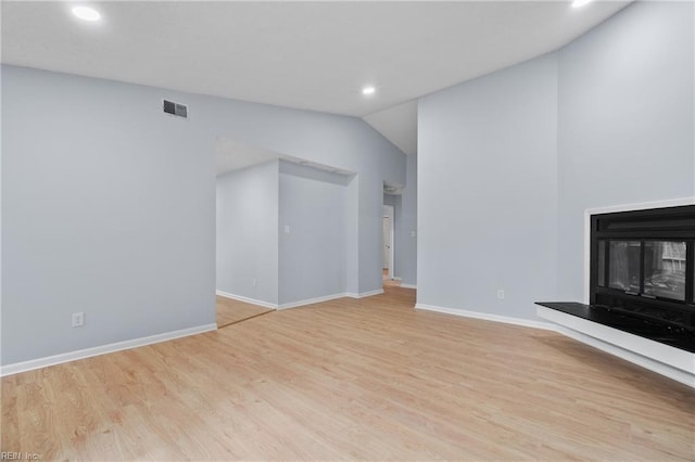 unfurnished living room featuring lofted ceiling, visible vents, a glass covered fireplace, wood finished floors, and baseboards