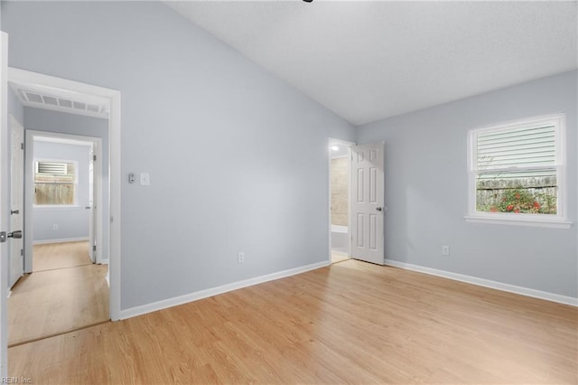 unfurnished bedroom featuring vaulted ceiling, multiple windows, light wood-type flooring, and baseboards