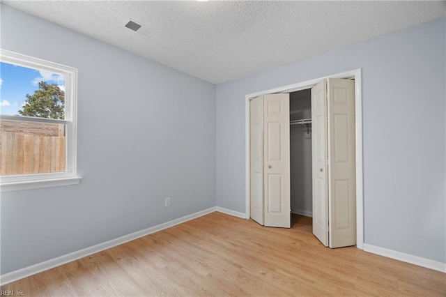 unfurnished bedroom with a textured ceiling, light wood-type flooring, visible vents, and baseboards