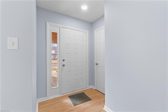 entryway featuring light wood finished floors, baseboards, and a textured ceiling