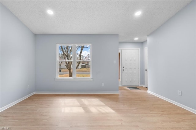 empty room with recessed lighting, light wood-style flooring, baseboards, and a textured ceiling