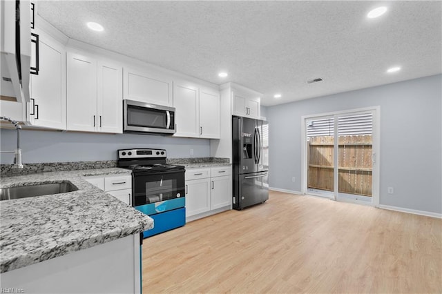 kitchen with appliances with stainless steel finishes, light wood-style floors, white cabinets, a sink, and a textured ceiling