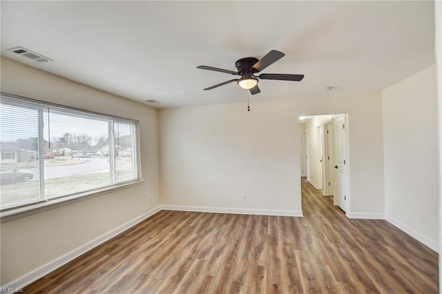 empty room featuring a ceiling fan, wood finished floors, visible vents, and baseboards