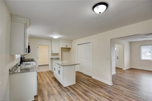 kitchen featuring a sink, baseboards, light wood-type flooring, a center island, and stainless steel microwave