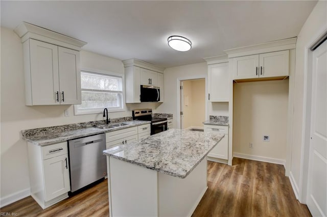 kitchen featuring light stone counters, stainless steel appliances, wood finished floors, a sink, and a center island