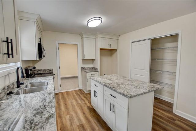 kitchen with light stone counters, white cabinetry, a sink, wood finished floors, and baseboards