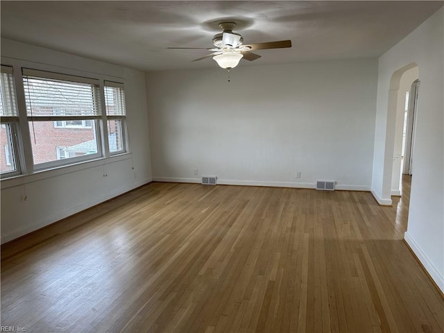 empty room featuring wood finished floors, arched walkways, visible vents, and baseboards