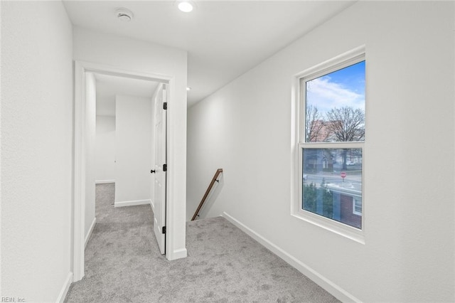 corridor with baseboards, light colored carpet, and an upstairs landing