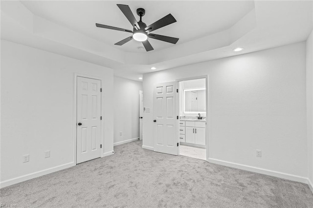 unfurnished bedroom with ensuite bathroom, baseboards, a raised ceiling, and light colored carpet