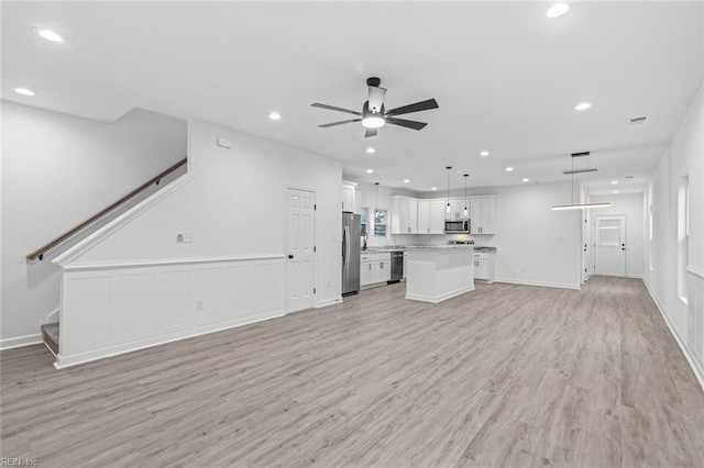 unfurnished living room featuring baseboards, a ceiling fan, light wood-style flooring, stairs, and recessed lighting