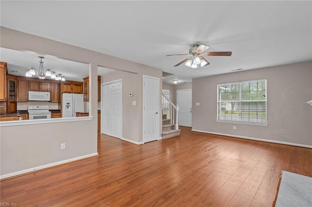 unfurnished living room featuring stairway, a sink, wood finished floors, baseboards, and ceiling fan with notable chandelier