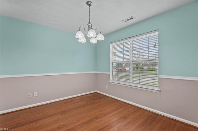 spare room featuring a chandelier, visible vents, baseboards, and wood finished floors