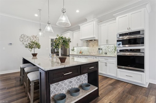 kitchen featuring double oven, dark wood finished floors, ornamental molding, and decorative backsplash