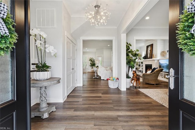 entrance foyer featuring visible vents, ornamental molding, wood finished floors, a lit fireplace, and a notable chandelier