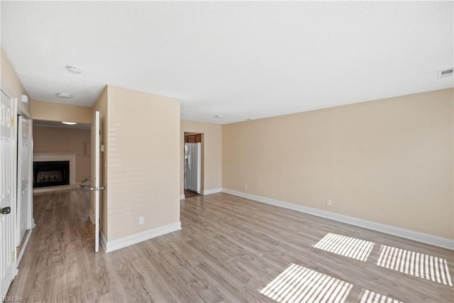 empty room with light wood-type flooring, a fireplace, and baseboards