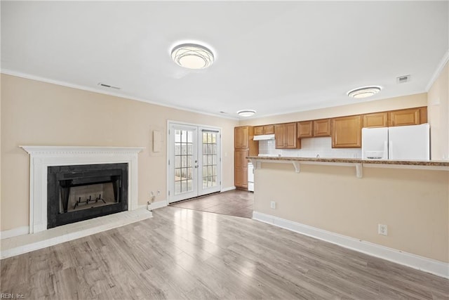 unfurnished living room featuring baseboards, a fireplace with raised hearth, light wood-style flooring, crown molding, and french doors