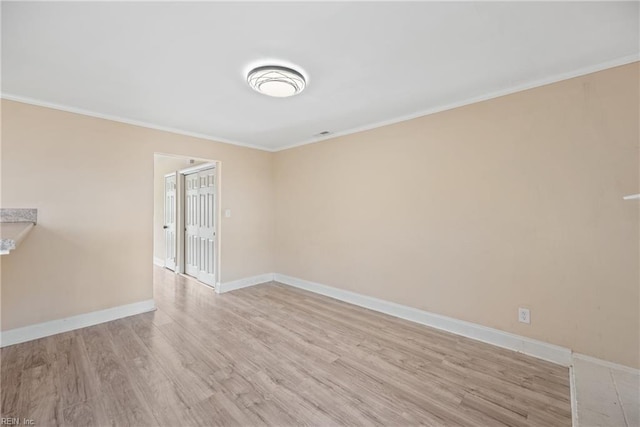 empty room with crown molding, light wood-type flooring, and baseboards