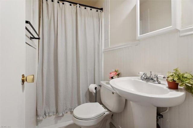 bathroom with a shower with shower curtain, a wainscoted wall, toilet, and a sink