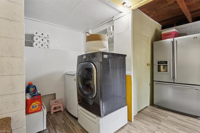 clothes washing area with laundry area, wood finished floors, concrete block wall, and separate washer and dryer